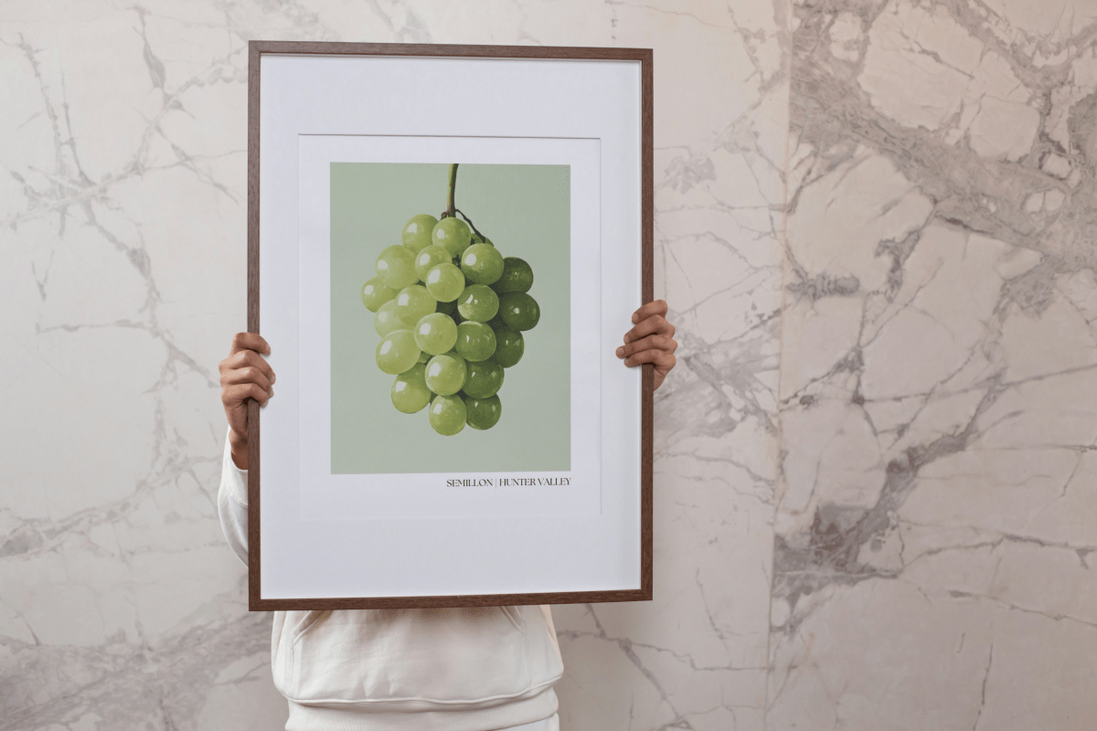 Person holding a framed Thirsty Merchy Semillon grape poster in front of a marble wall. The poster highlights Hunter Valley’s renowned wine culture, available for purchase online. A collaboration with Stay n' Sip, promoting luxury wine-tasting experiences and elegant home decor.