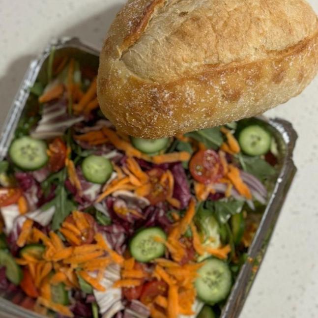 Freshly prepared salad with vibrant vegetables, including cucumbers, carrots, cherry tomatoes, and mixed greens, served alongside a rustic loaf of artisan bread. Part of Stay n' Sip's gourmet meal delivery service, designed to complement wine tasting experiences