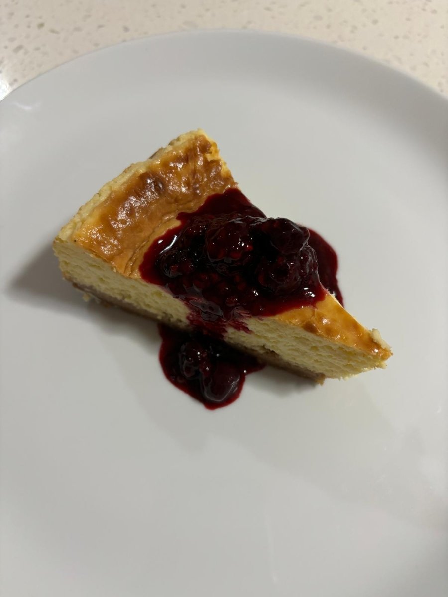 Slice of creamy baked cheesecake topped with a rich berry compote, served on a white plate. A decadent dessert option from Stay n' Sip's gourmet meal delivery service, designed to pair perfectly with premium Hunter Valley wines