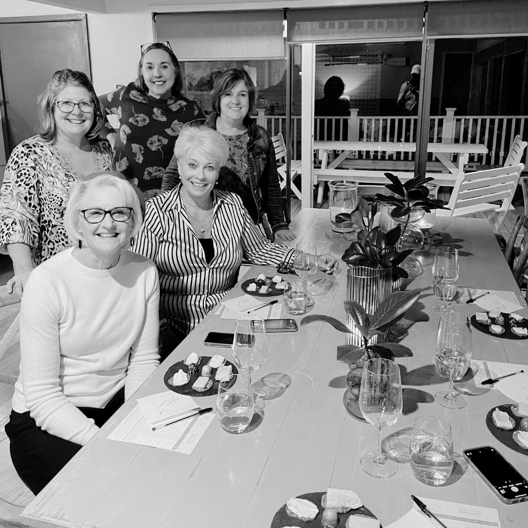 Group of guests enjoying a Stay n’ Sip Gourmet Wine Tasting experience, seated around a table with wine glasses and gourmet cheese plates, reflecting the refined and intimate nature of the tasting