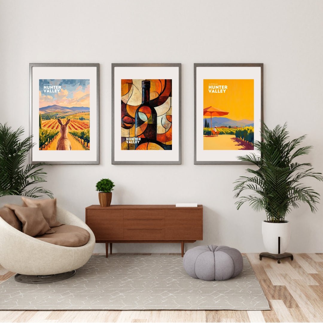 A set of three framed Thirsty Merchy posters displayed in a stylish modern living room. The artworks include a kangaroo overlooking Hunter Valley vineyards, an abstract wine bottle design, and a vibrant vineyard scene with a red umbrella. These posters celebrate Hunter Valley's wine culture and are part of Stay n' Sip's exclusive art collection, available for purchase online