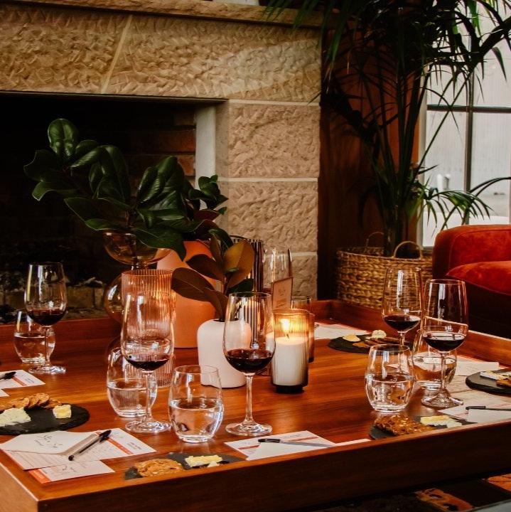 Table set for a wine tasting with glasses, cheese plates and tasting notes in front of a fireplace.