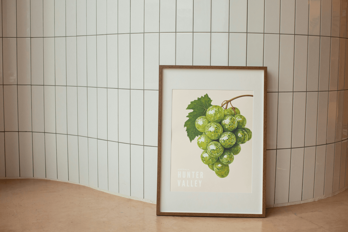 Framed Thirsty Merchy poster featuring a vibrant cluster of green grapes with a leaf, resting against a tiled wall. This modern artwork highlights Hunter Valley’s renowned wine culture and is part of Stay n' Sip's exclusive collection, available for purchase online