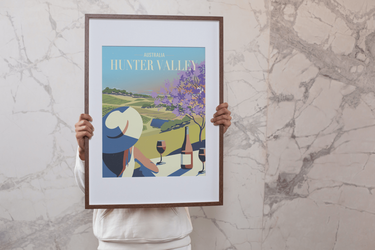 Person holding a framed Hunter Valley Bistro Sunset Poster, showcasing a stylish and scenic illustration of wine culture in Hunter Valley, perfect for home or office decor