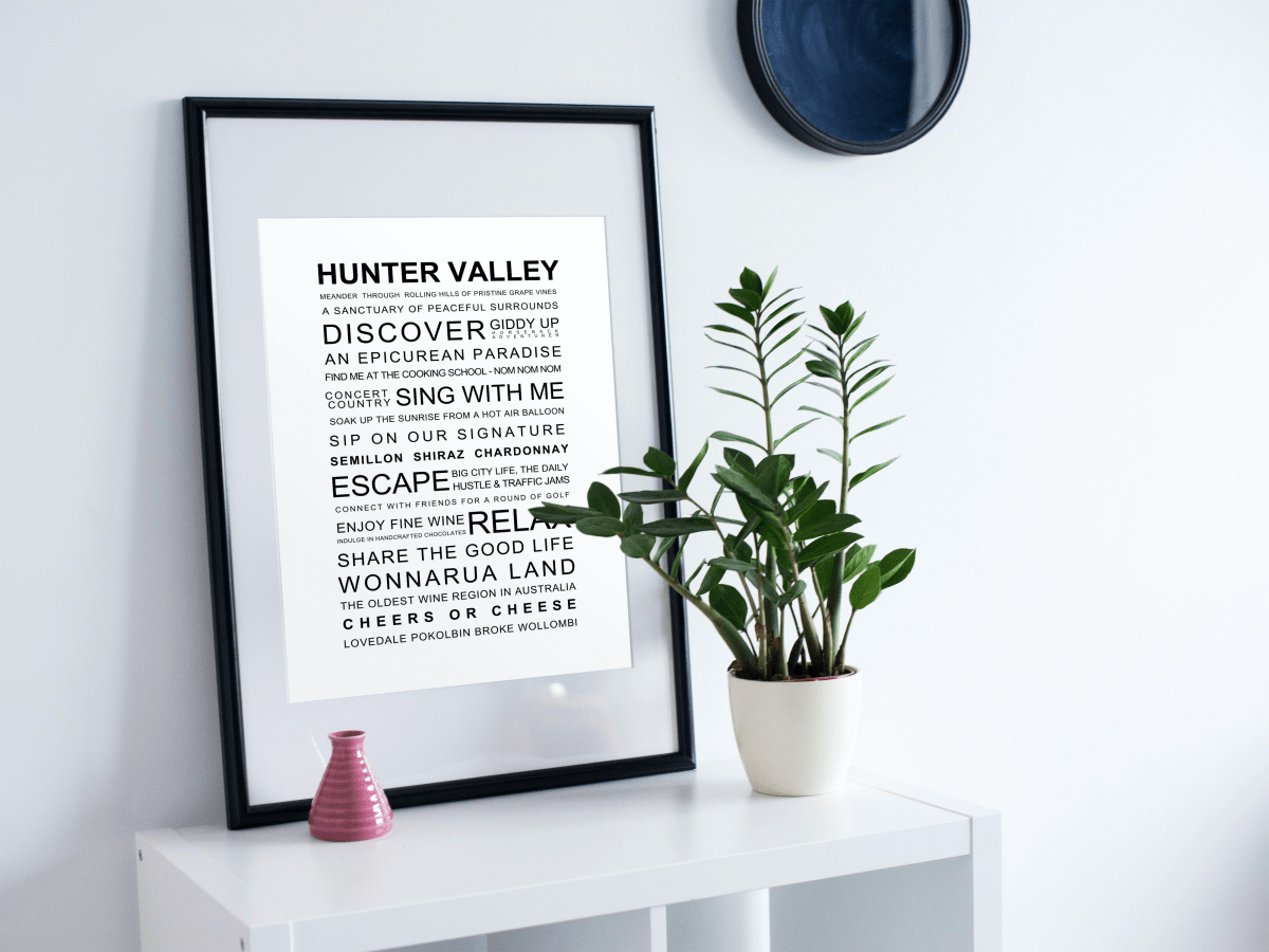 Framed Hunter Valley Experience Poster displayed on a white shelf with a modern plant and decorative pink vase, set against a minimalistic white wall