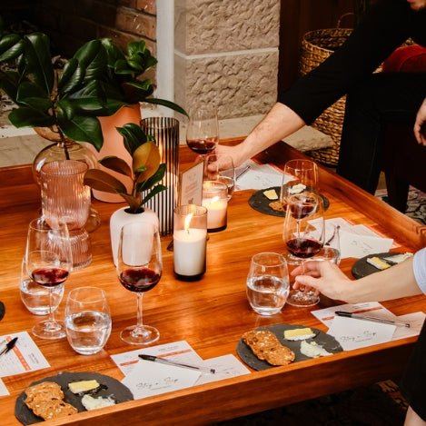 Cozy private wine tasting setup by Stay n’ Sip, featuring red wine glasses, cheese plates, candles, and personalized tasting notes, ideal for intimate gatherings at home or accommodation