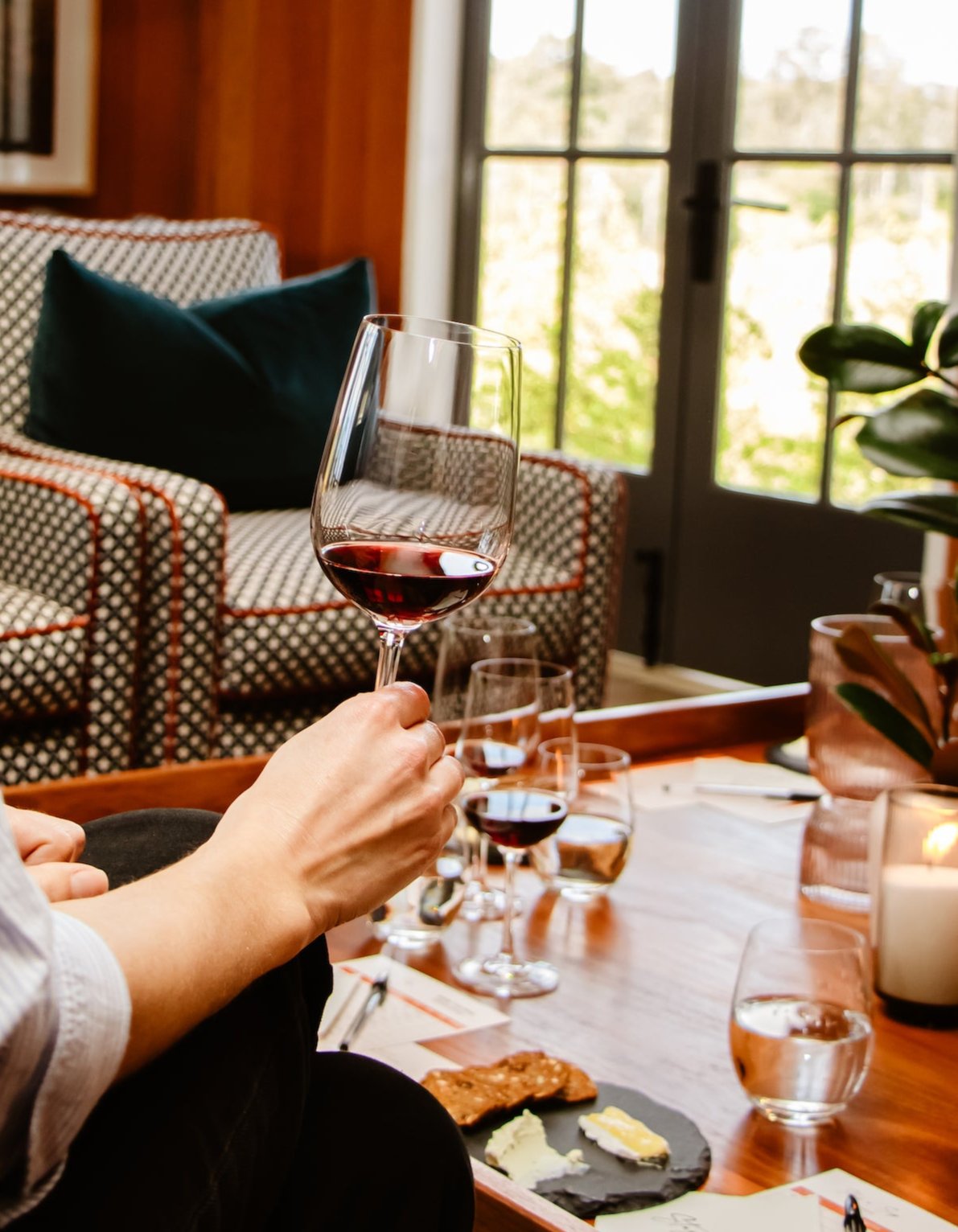 Person enjoying a glass of red wine during a private wine tasting in a cozy setting. The beautifully set table features cheese pairings, showcasing Stay n' Sip's best in-house wine tasting experiences, perfect for a relaxed and luxurious atmosphere.