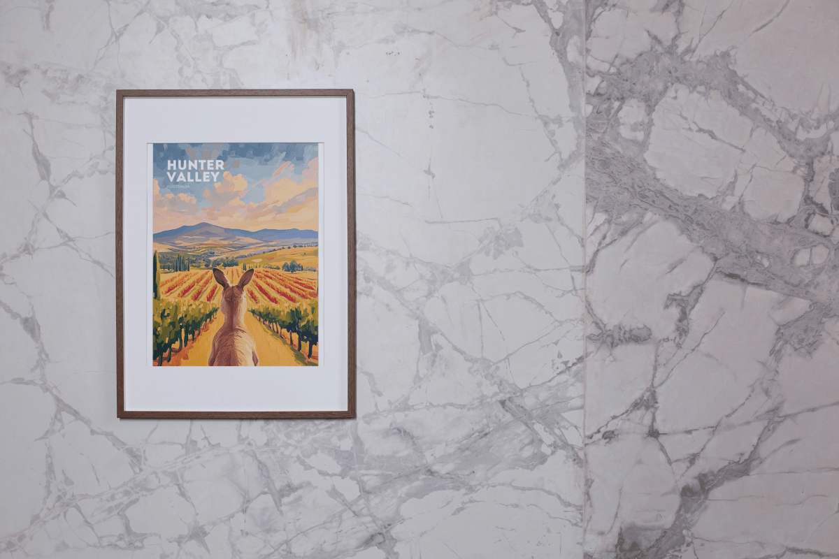 Framed poster of a kangaroo overlooking colorful vineyards in Hunter Valley, Australia, displayed on a marble wall. This Thirsty Merchy artwork celebrates the region's natural beauty and wine culture, available as part of Stay n' Sip's exclusive collection for purchase online